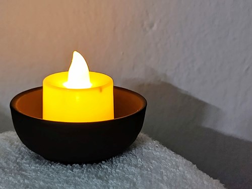 LED candle lit in a bowl on a fabric surface.