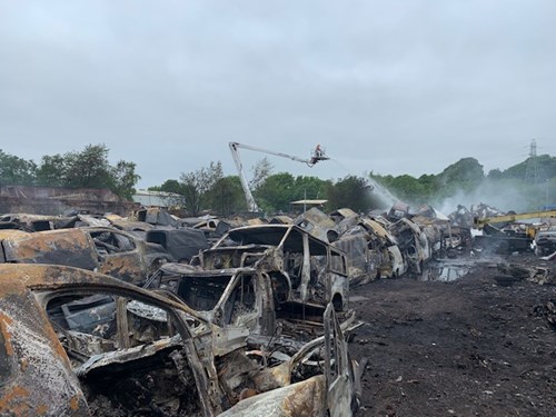 A scene of a salvage yard filled with burned-out vehicles, many charred and blackened