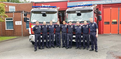 Group of firefighters stood in front of two fire engines