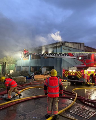 Two firefighters in PPE in front of building on fire