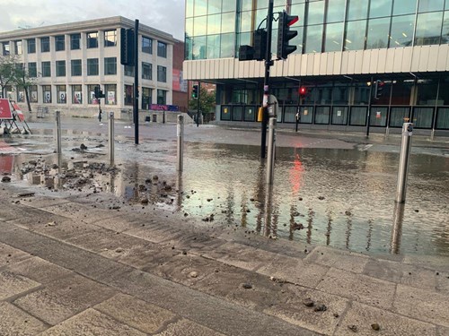 Flooded Oxford Road in Manchester with debris and modern buildings in the background