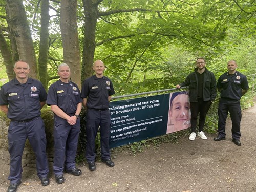 A group of four firefighters with Chris Jordan, the uncle of Jack Pullen stand next to a water safety banner dedicated to Jack Pullan urging others not to swim in open water, while engaging with the community