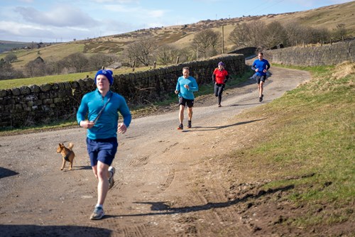 Runners pass along a route by a dry stone wall, with hills in the background
