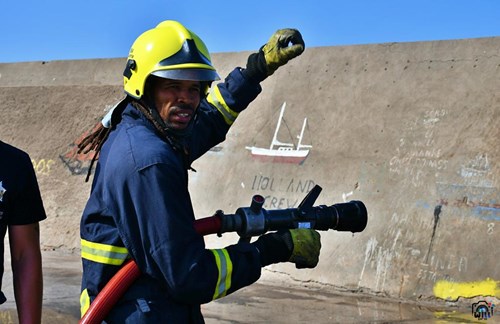 A firefighter holds a hose and looks over his shoulder into the camera