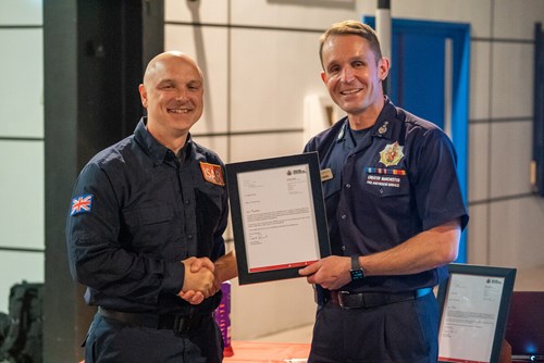 Chief Fire Officer Dave Russel presents Martin Foran with a certificate. Both look into the camera and smile.