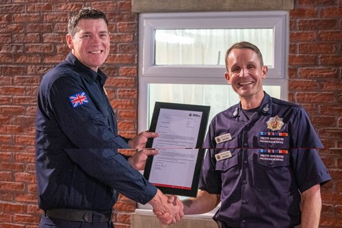 Chief Fire Officer Dave Russel presents Steven Pennington with a certificate. Both look into the camera and smile