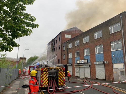 Firefighters using hoses to battle flames at a derelict mill with smoke coming from the building