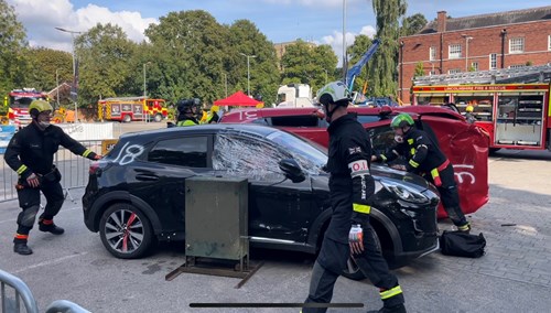 A group of emergency responders in helmets and safety gear performing a vehicle extrication exercise involving a damaged car