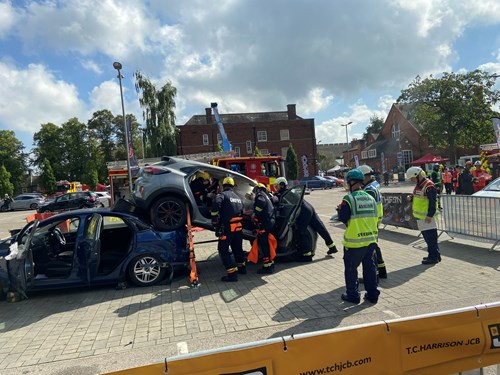 A group of emergency responders in helmets and safety gear performing a vehicle extrication exercise involving overturned and damaged cars