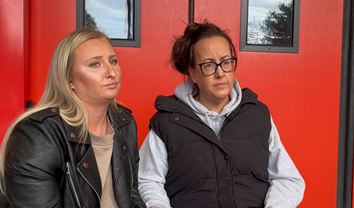 Two people wearing coats in front of a red door looking forwards.