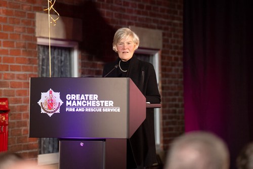 Deputy Mayor Kate Green stood at a lectern with the GMFRS logo on the front. She is addressing a crowd in the room.