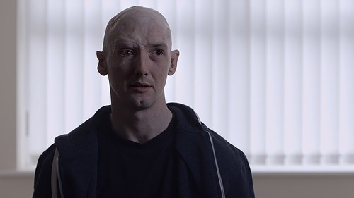 Concerned-looking man Gary Walker in a dark hoodie stands in front of vertical blinds, creating a dramatic atmosphere