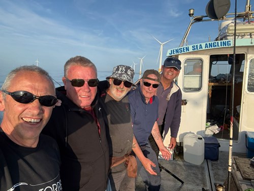 Five men stood on the back of a fishing boat, with their arms around one another smiling directly for the camera.