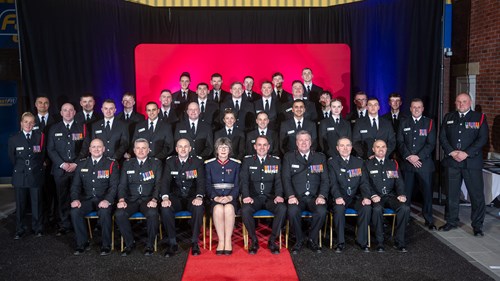 Group photo of 24 new GMFRS firefighters sat and stood in rows along with other GMFRS staff members and King's representative – all facing the camera smiling